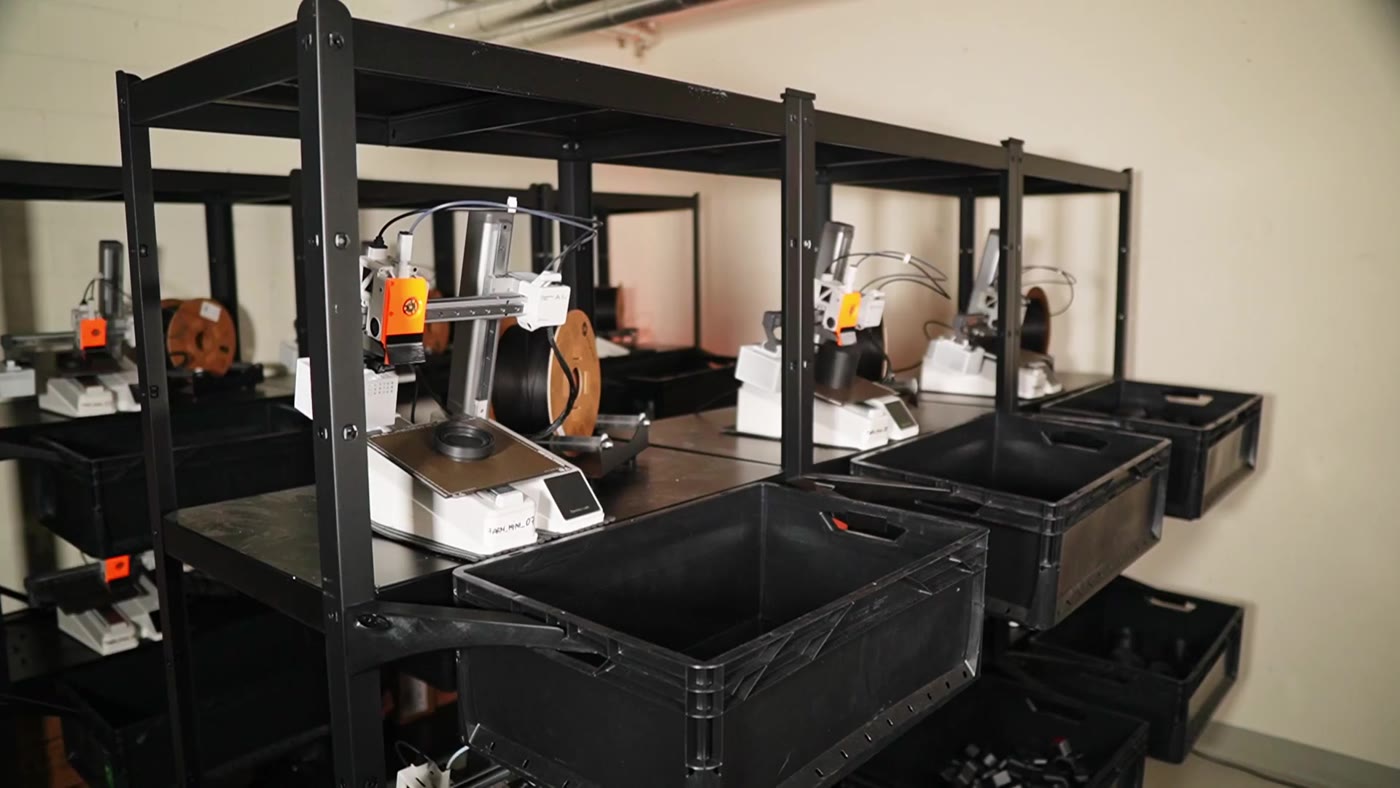 A rack of Bambu Lab printers with finished parts dropping into collection bins on the floor at the 3D Farmers print farm