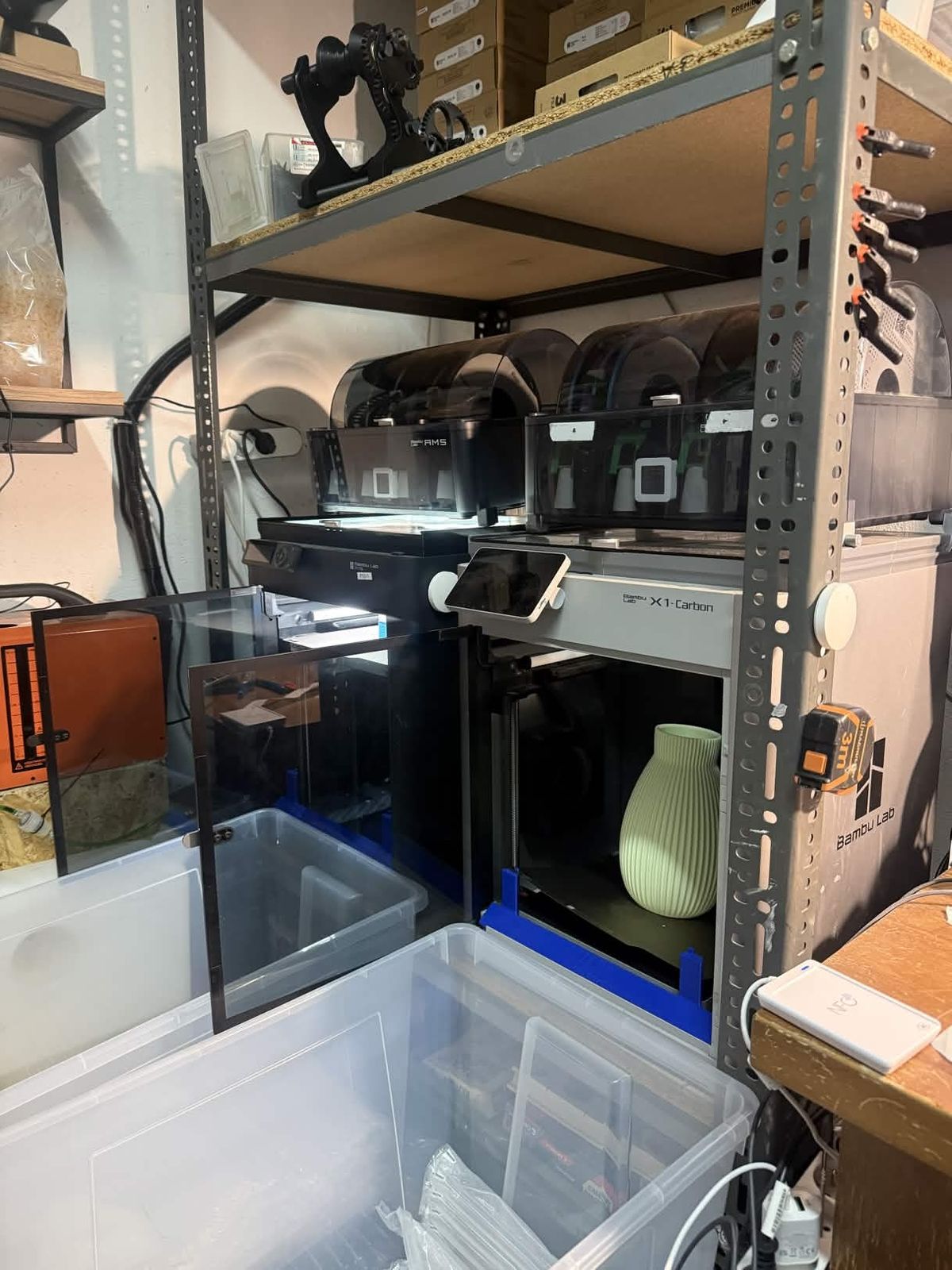 A real Bambu Lab X1-Carbon with AMS on Patryk's workshop shelving, a green vase printing in the chamber