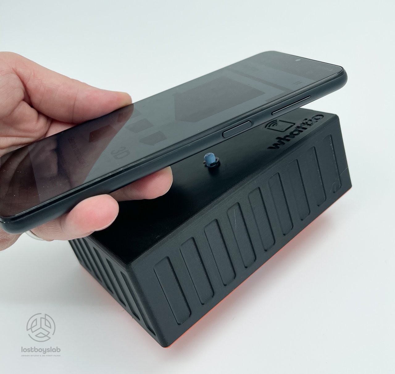 A hand tapping a phone against a 3D-printed whatt.io enclosure to read its NFC product passport
