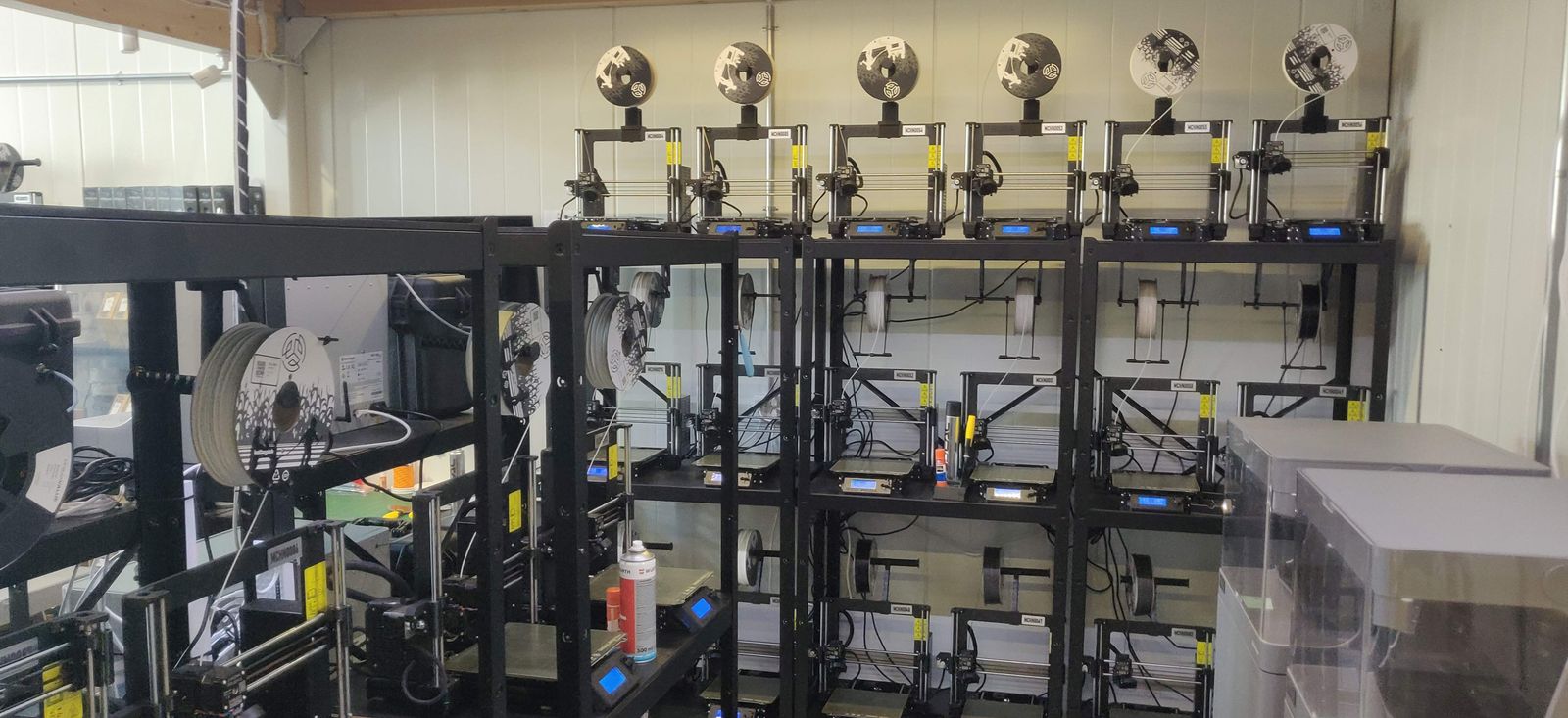 Rows of Prusa printers on rack shelving with branded recycled spools feeding from above