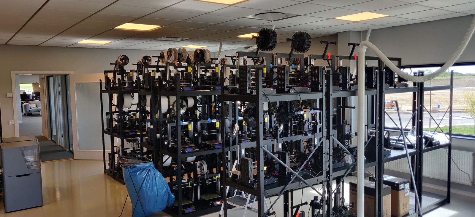 Rear view of the large printer rack in a bright room with windows and overhead exhaust ducting