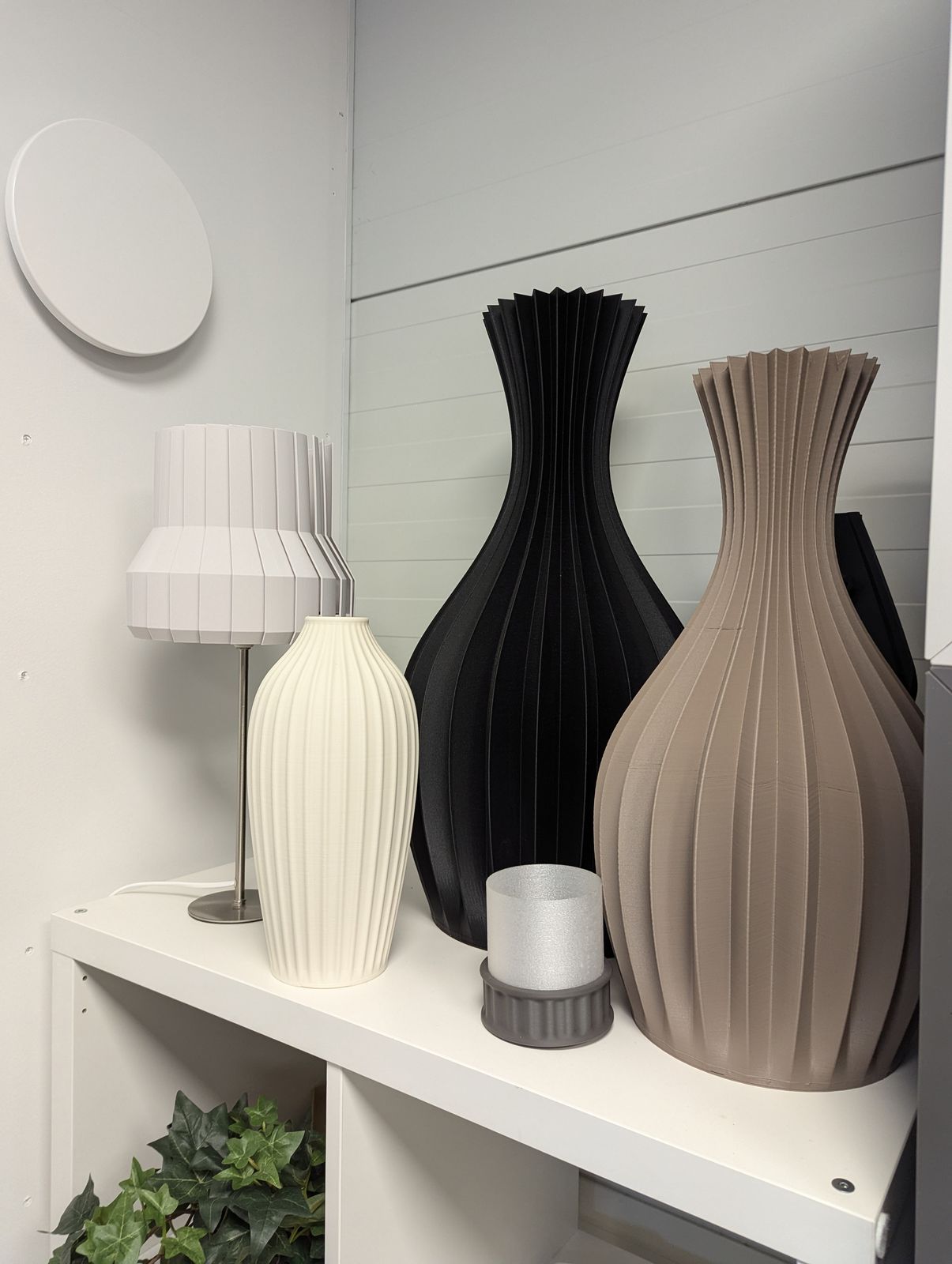 A shelf of fluted 3D-printed vases in white, black and taupe, with a printed table lamp
