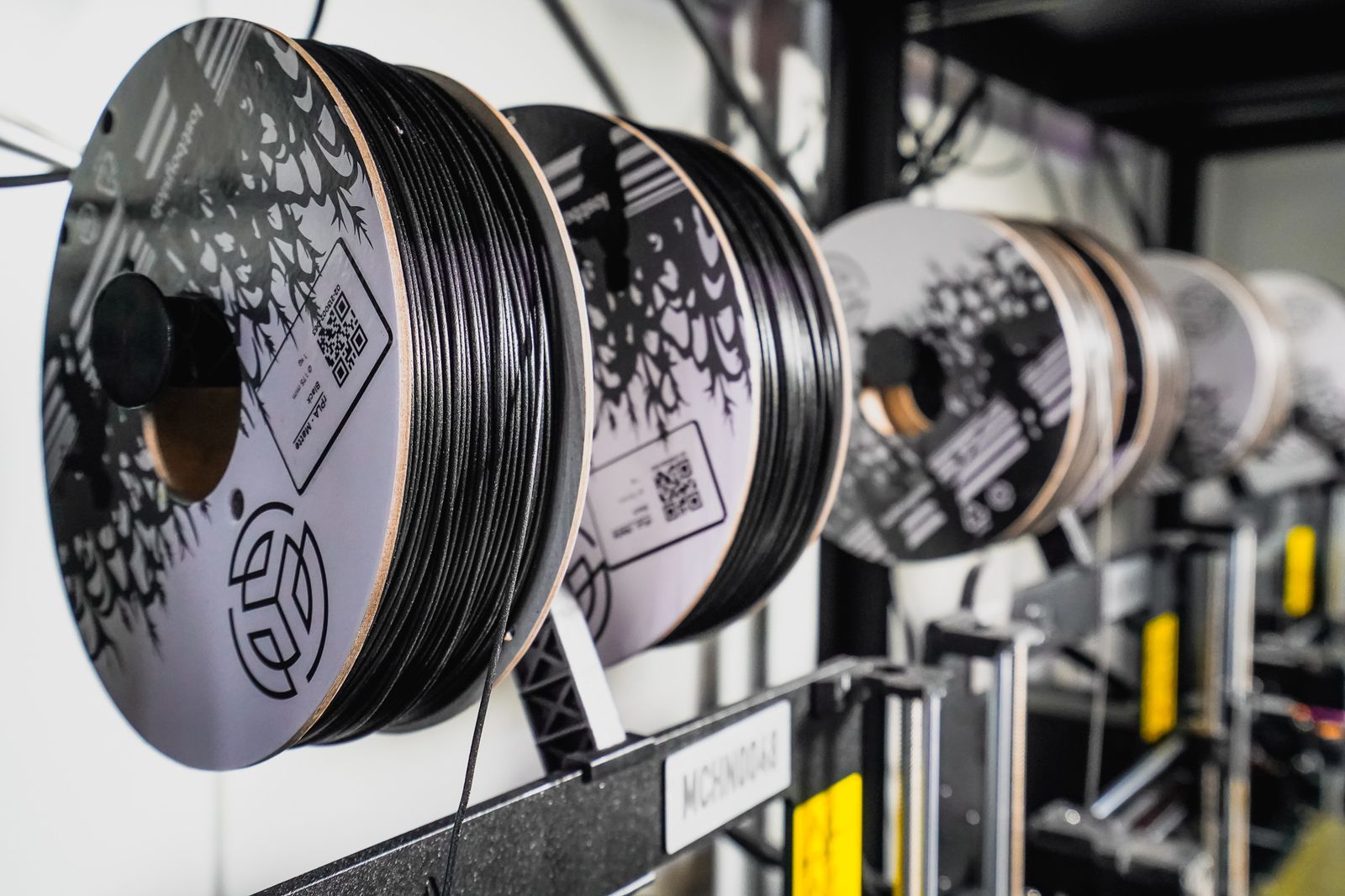 A row of black recycled-filament spools with branded artwork on the cardboard sides and QR batch labels