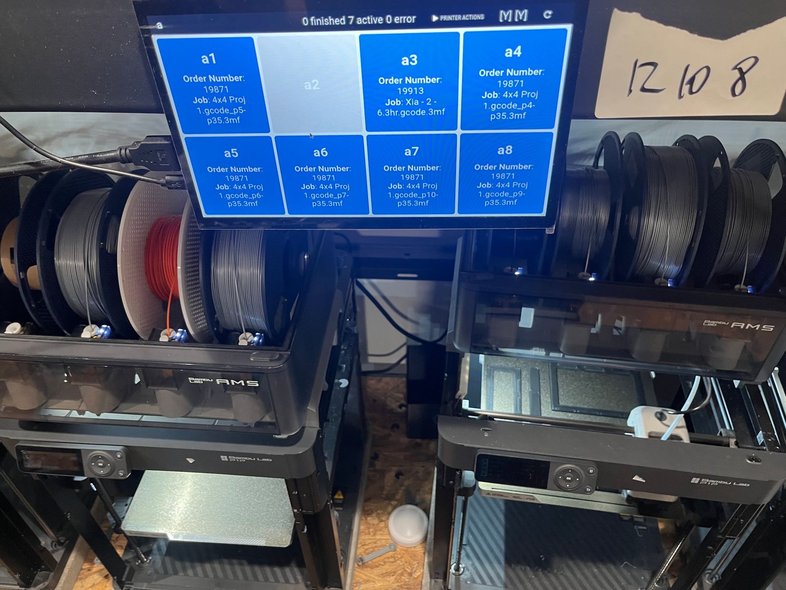 A SimplyPrint Display order-grid screen showing job slots a1-a8 with order numbers and filenames, mounted above two Bambu Lab P1 printers with external AMS spools