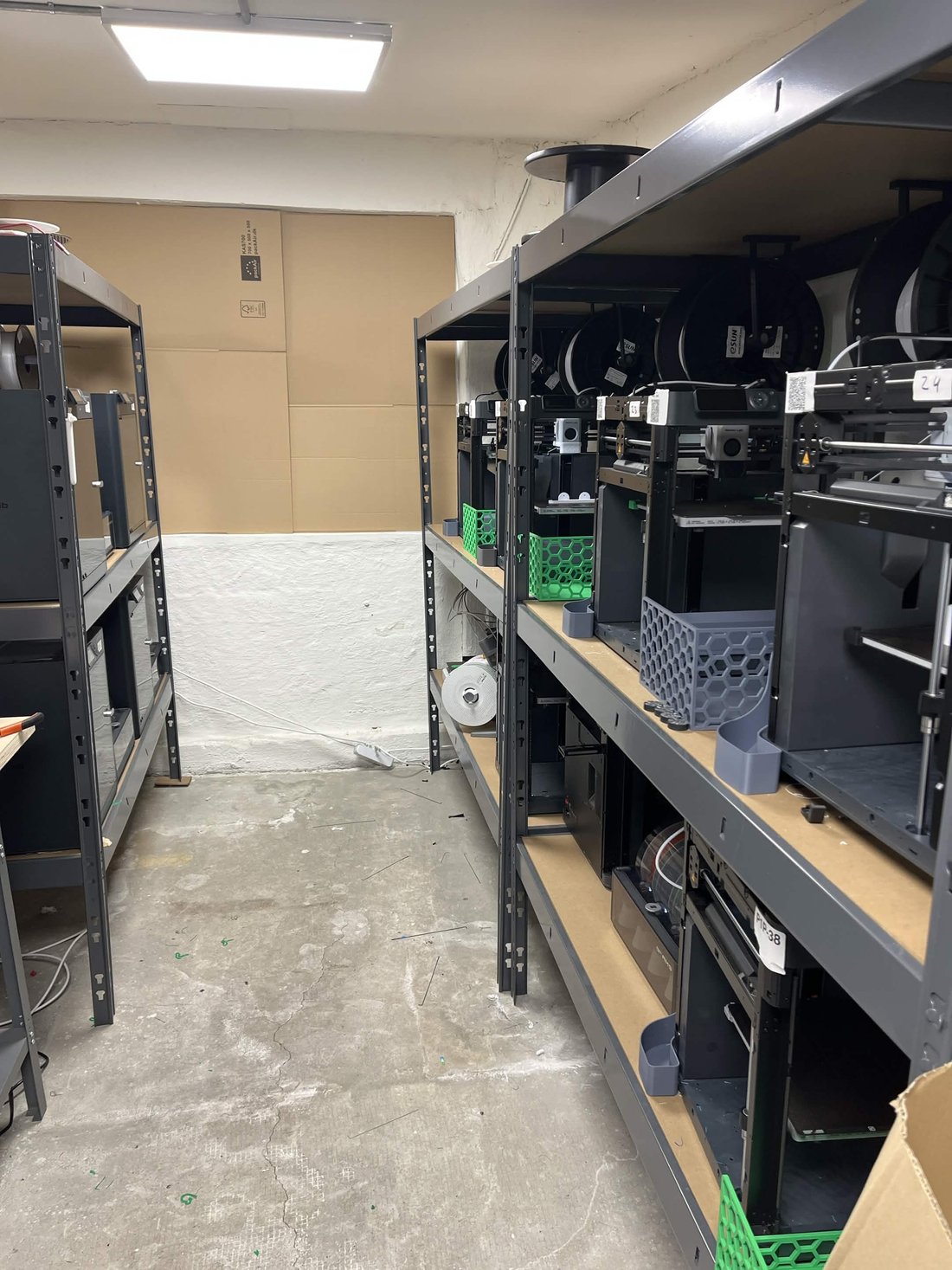 An angled view of Weshape's shelving with Bambu Lab P1P printers, filament spools on top and 3D-printed organiser baskets
