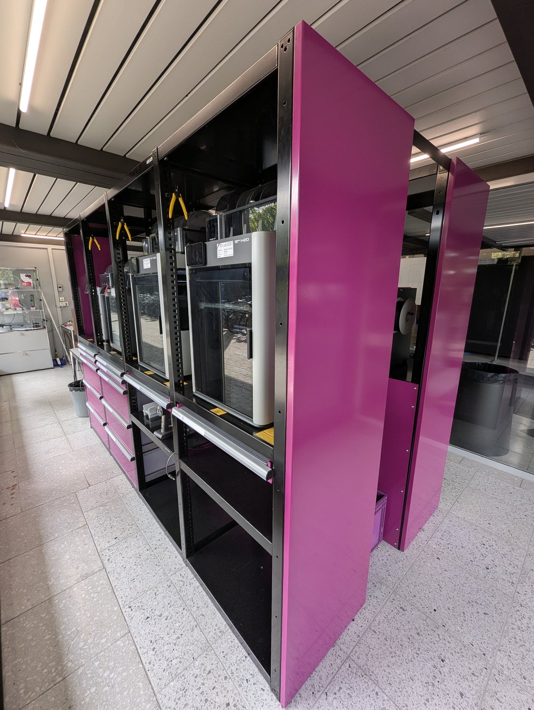 Glossy magenta printer cabinets in the OST 3D-Lab seen from the side, enclosed Bambu Lab printers in the bays