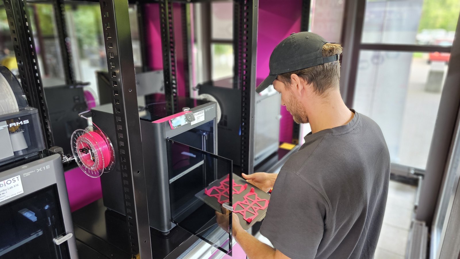 A student in the OST 3D-Lab lifting a build plate of fresh magenta 3D prints off a Bambu Lab printer